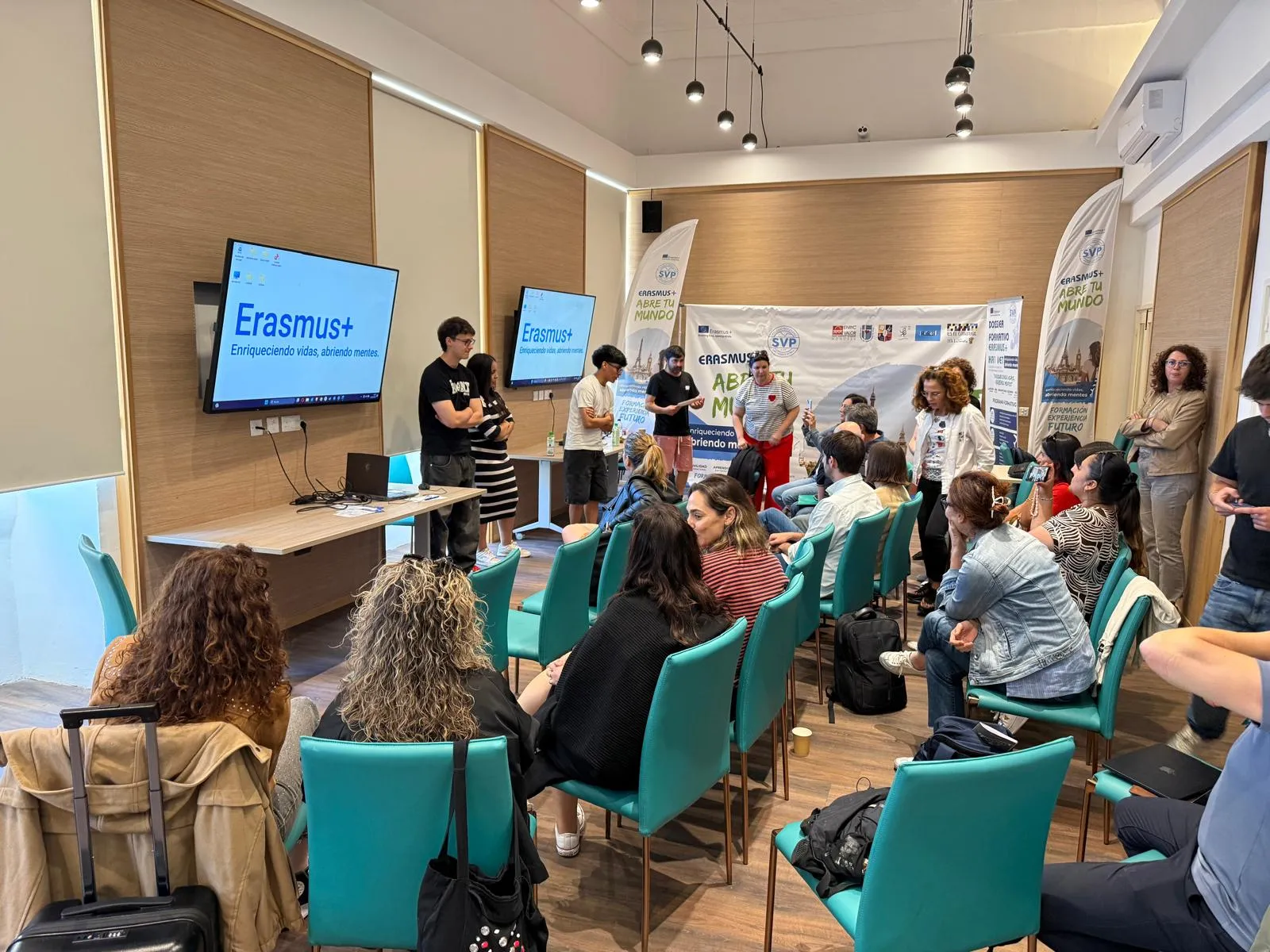 Students presenting in front of a screen with the Erasmus+ motto to a seated audience